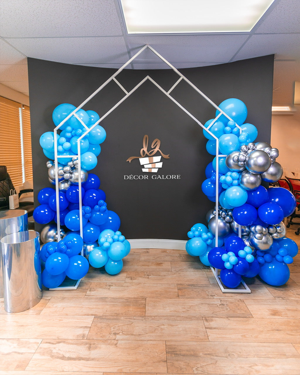 Decorative balloon arch with blue and silver balloons against a black backdrop with 'Decor Galore' logo.
