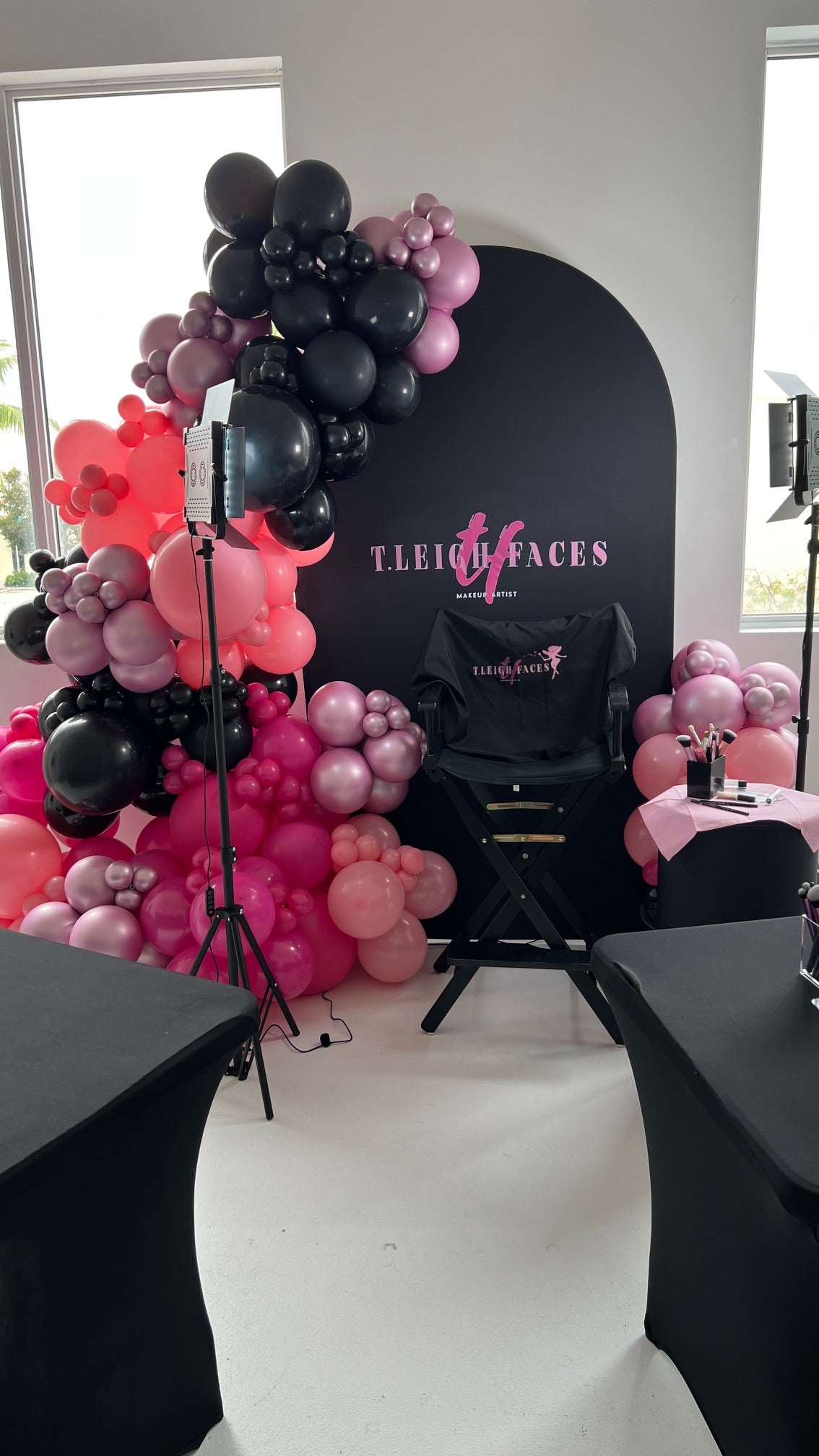 Decorative balloon arch with pink and black balloons in front of a branded backdrop.